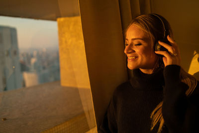 Woman listens to music with headphones by the window with a city view. mobile phone, technology, 