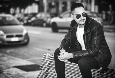 Young man sitting on car in city