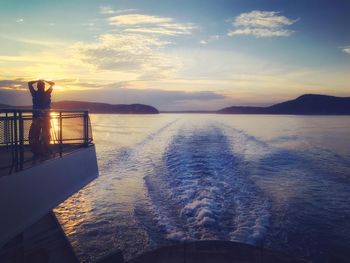 Man on boat in sea against sky during sunset