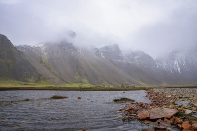 Close-up of stream flowing amidst grassy field against vestrahorn mountain