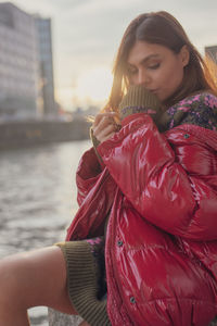 Side view of young woman wearing warm clothing against river in city
