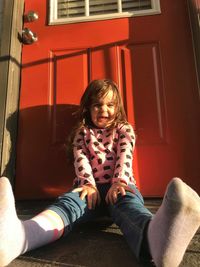 Portrait of cheerful girl sitting against closed red door