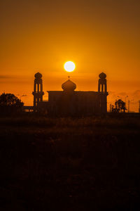 Silhouette tower on field against sky during sunset