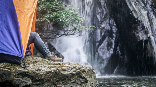 Low section of man sitting in tent by waterfall