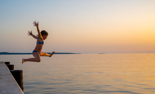 Side view of man jumping in sea against sky during sunset