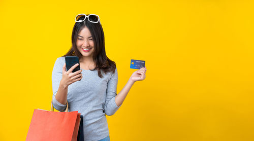 Smiling young woman using mobile phone against yellow background