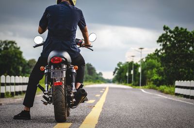 Rear view of man riding motorcycle on road against cloudy sky