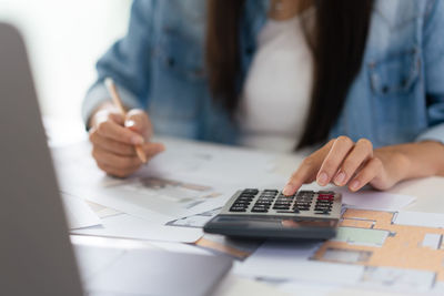 Design building concept, female architect is using calculator and sketching house plan on blueprint.