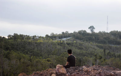 Rear view of man standing on rock against sky