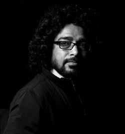 Portrait of young man with curly hair wearing eyeglasses while standing against black background