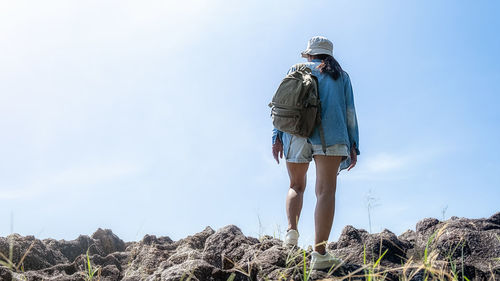 Rear view of woman standing on rock against sky