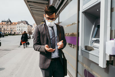 Man holding mobile phone while standing on laptop