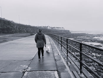 Rear view of woman walking on footpath by sea