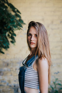 Portrait of young woman standing by wall