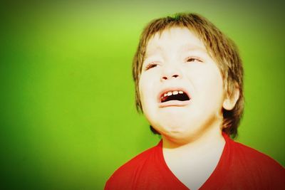 Close-up of boy crying against green background