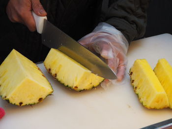 Cropped image of male vendor cutting pineapple on board