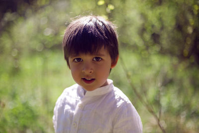 Caucasian child boy in a white shirt stands outdoors in the garden on a background of grass