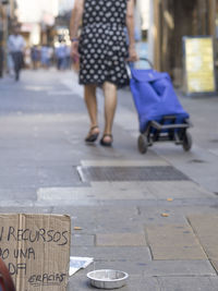 Text on box by container at sidewalk with woman walking in background