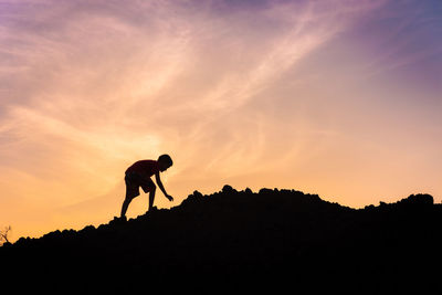 Silhouette boy on hill against sky during sunset