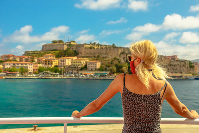 Woman looking at sea by cityscape against sky