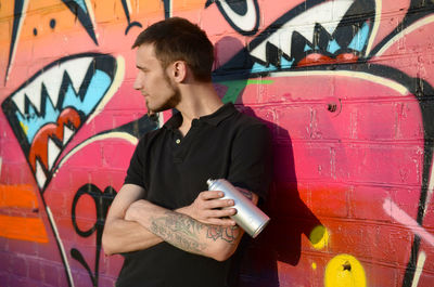 Full length of young man standing against graffiti wall