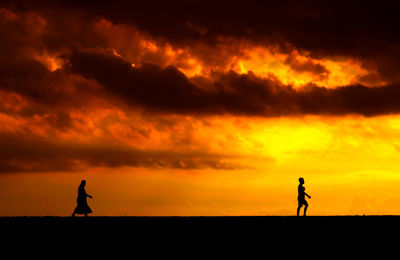 Silhouette people walking on field against orange sky