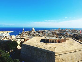 High angle view of townscape by sea against blue sky