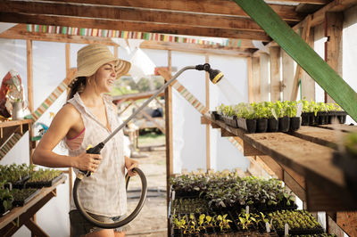 Happy female farmer watering seedling trays in greenhouse