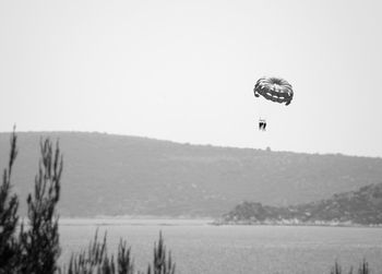 Person paragliding over landscape against clear sky