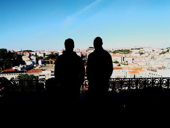 Rear view of silhouette men sitting in city against clear sky