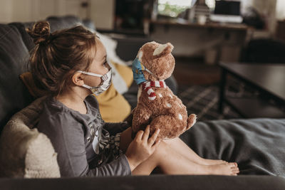 Side view of preschool age girl with mask on cuddling masked animal