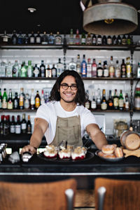 Portrait of smiling confident young owner with dessert standing at counter in restaurant