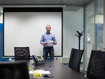 Portrait of businessman standing by projection screen in board room at office