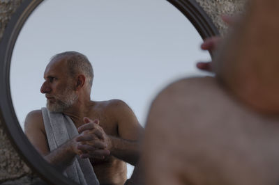 Shirtless adult man looking away in mirror