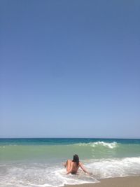 Rear view of couple on beach against clear blue sky