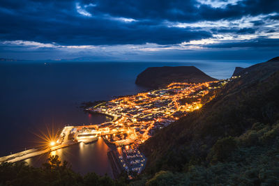 Aerial view of illuminated city by sea against sky