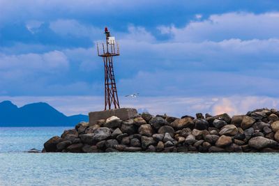 Lookout tower by sea against cloudy sky