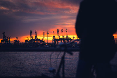 Silhouette cranes by sea against sky during sunset