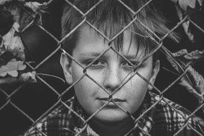 Close-up of boy standing by chainlink fence