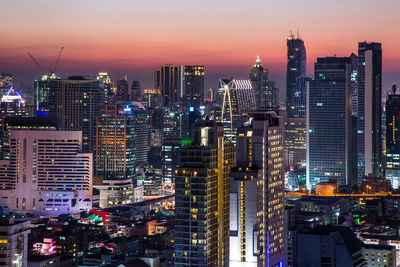 Illuminated buildings in city against sky during sunset