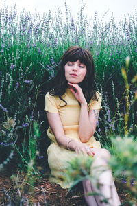 Young woman looking away while sitting on field