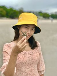 Portrait of woman wearing hat holding starfish standing at beach