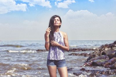 Young woman standing on beach against sky