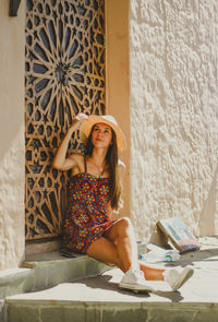 Fashionable young woman sitting against wall