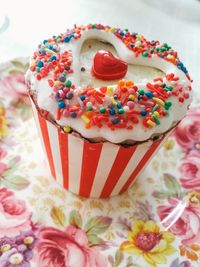 High angle view of cupcake with colorful sprinkles and heart shape icing in floral plate