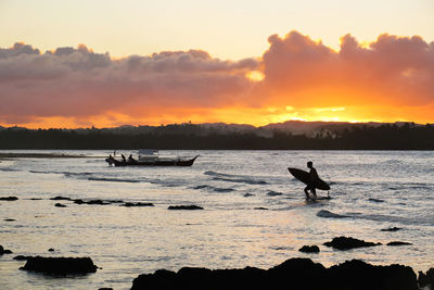 Silhouette surfer in sea against sky during sunset