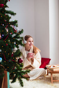 Young woman sitting next to christmas tree at home