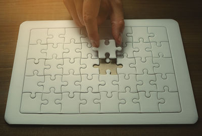 High angle view of person hand holding jigsaw piece by puzzle on table