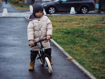 Cute toddler boy in stylish skirt riding on his balance bike at autumn park