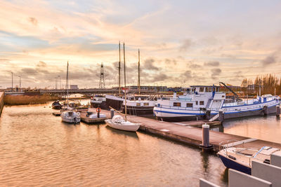 Boats moored in harbor at sunset